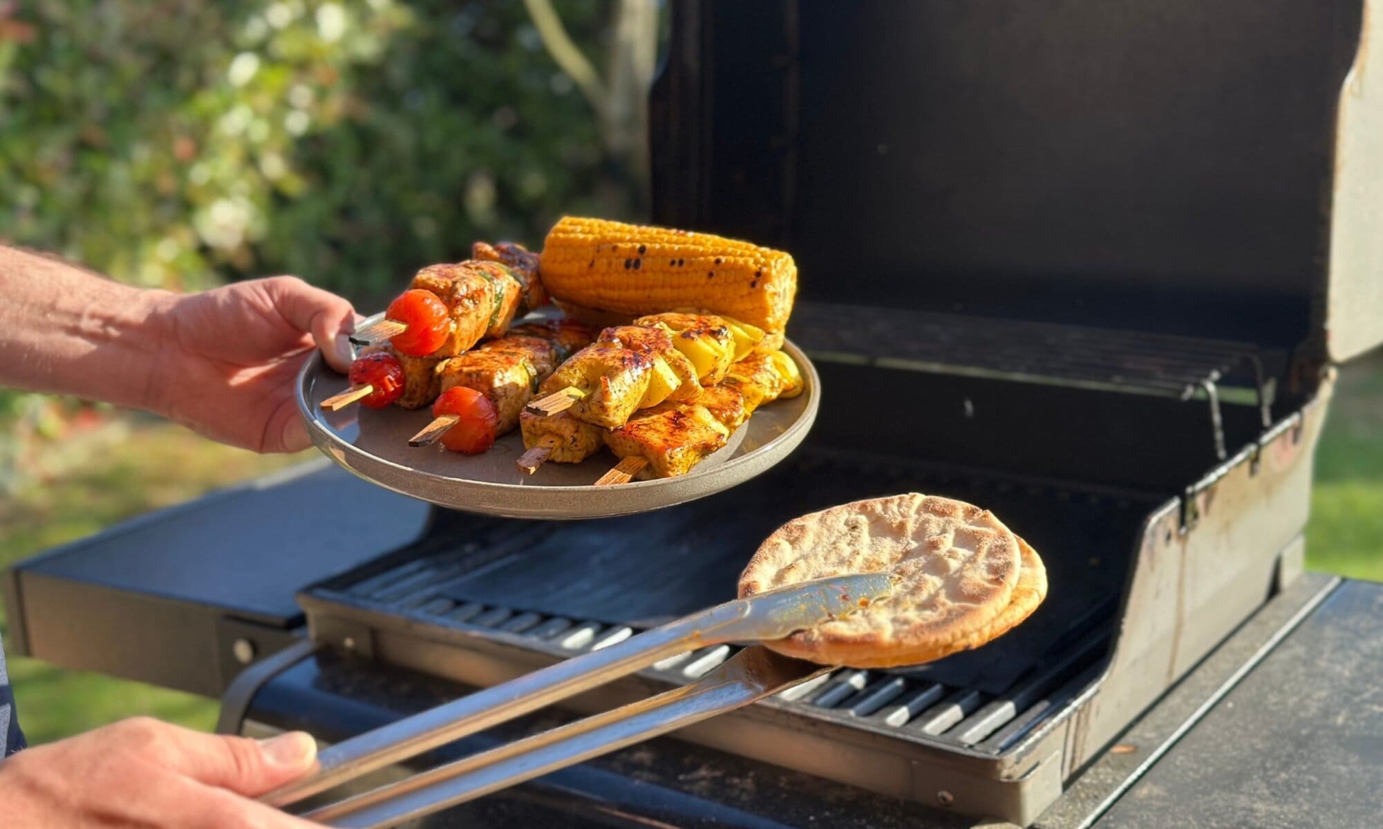 Glutenfreie Pitas frisch vom Grill – sicher mit Grillmatte Grill mit Grillmatte im Hintergrund, auf dem Teller frisches Grillgut – in der Zange glutenfreie Pitas