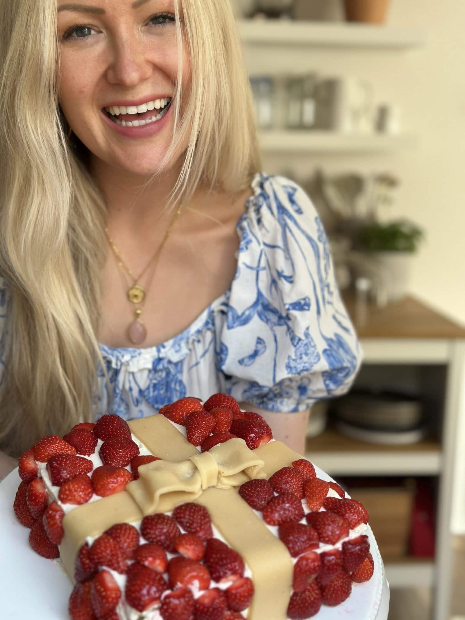 Glutenfreier Genuss – Aurélie mit Erdbeerkuchen in ihrer Küche Aurélie steht in ihrer Küche mit einem glutenfreien Erdbeerkuchen in der Hand und strahlt in die Kamera