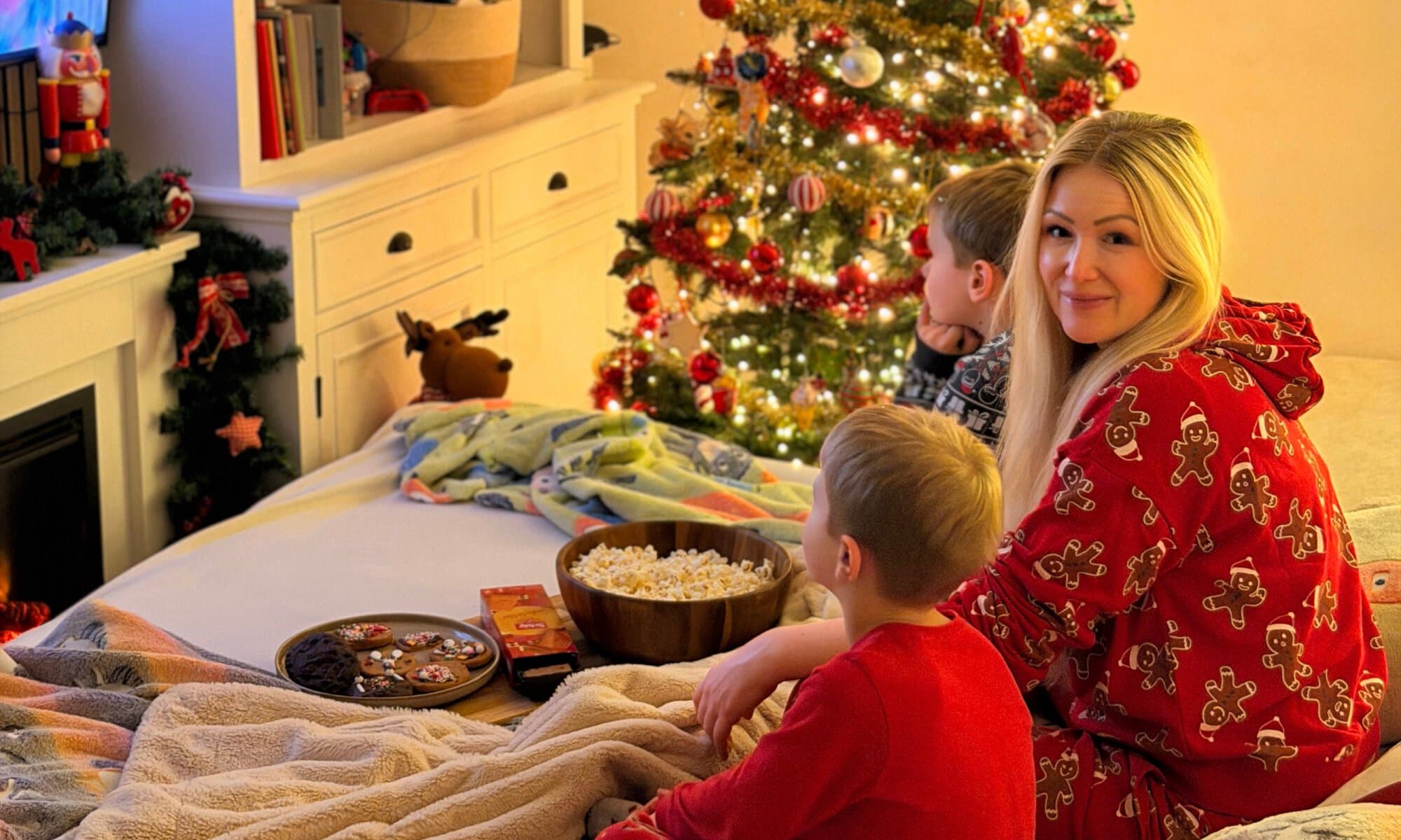 Aurélie sitzt mit ihren Kindern vor einem festlich geschmückten Weihnachtsbaum, trägt einen Lebkuchen-Schlafanzug und schaut gemeinsam einen Weihnachtsfilm. Vor ihnen stehen Popcorn, selbst dekorierte glutenfreie Cookies und Schär Spekulatius.