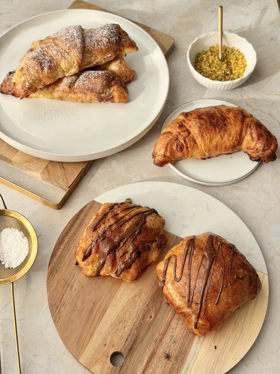 Glutenfreie Croissants und Pain au Chocolat auf weißen Tellern und Holzbrettchen stilvoll angerichtet
