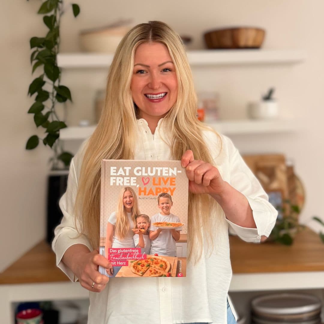 Glutenfreies Kochbuch für Familien mit Zöliakie – Autorin Aurélie Caudy hält ihr Buch in der Küche bei natürlichem Licht und lächelt in die Kamera